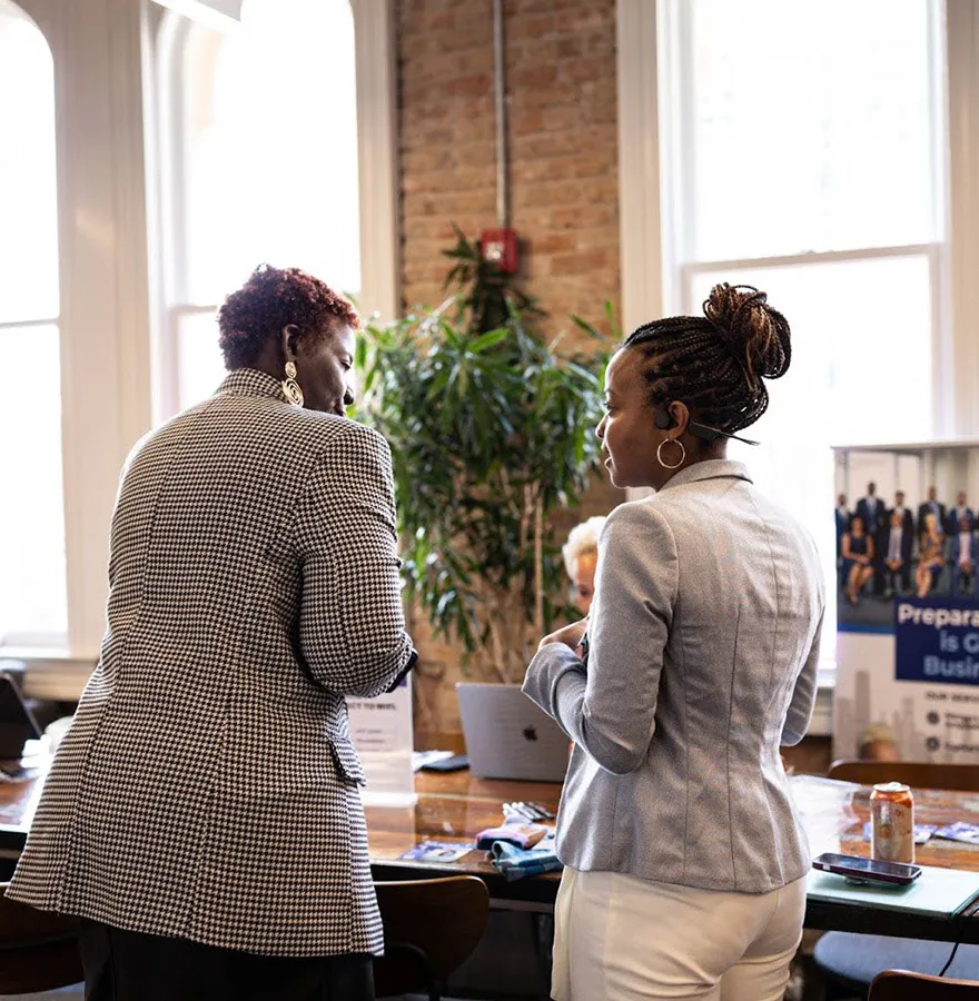 Two business women are talking in a brick office building.