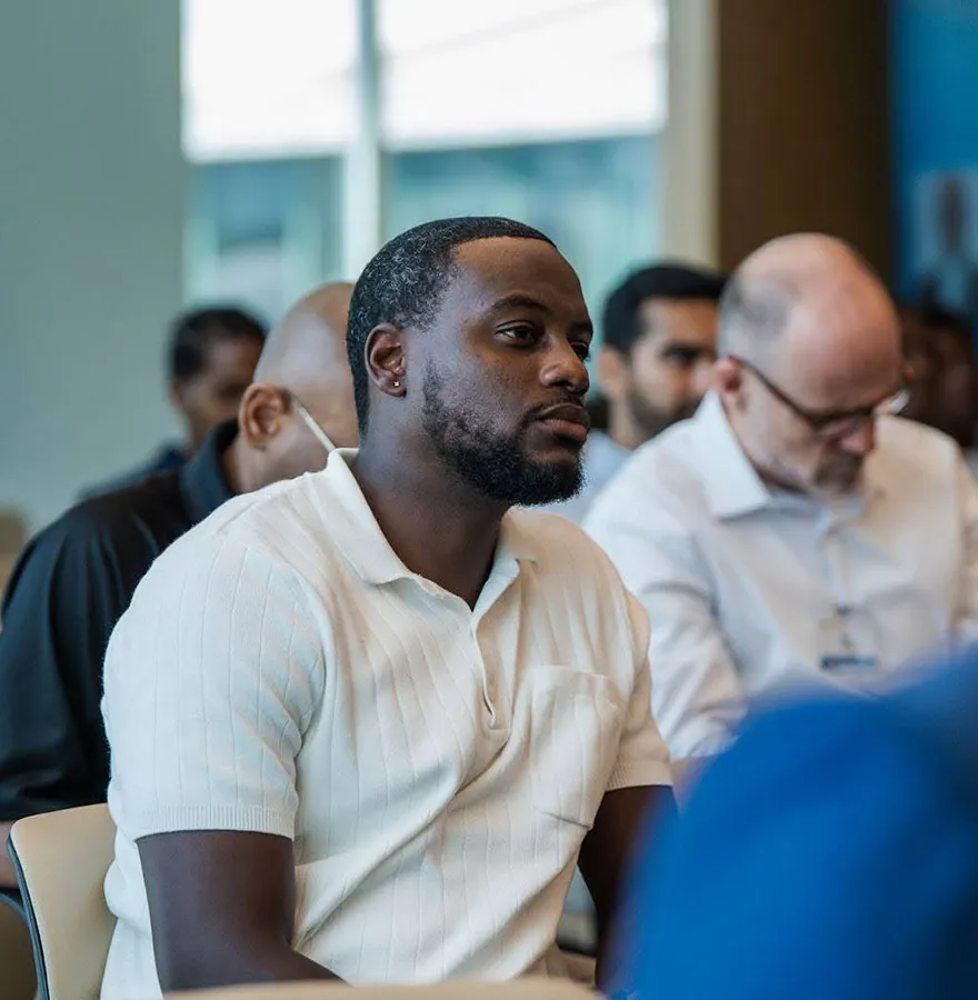 A man in sits attentively among a group of people during a seminar.