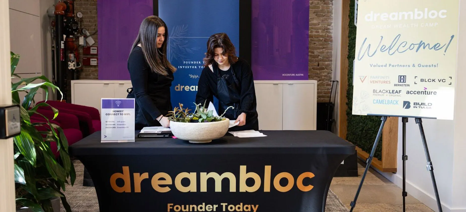 Two women stand behind a table at dreambloc event checking documents.
